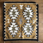 The "Two Grey Hills Rug" by Vintage features geometric Navajo-inspired patterns in white, olive green, gray, and black on a tan background, shown here laid on a wooden floor.