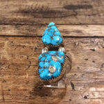 The Vintage Two-stone Turquoise Ring in size 8.5, crafted in sterling silver and featuring dark matrix patterns, is displayed on a rustic wooden surface.