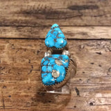 The Vintage Two-stone Turquoise Ring, size 8.5, showcases vibrant turquoise stones with dark veining, set against a rustic wooden background.