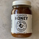 A 22-ounce jar of Weaver's Honey by R. Weaver Apiaries, featuring a white label with the R. Weaver Apiaries logo and text, sits on a light surface—a true taste of Texas honey.