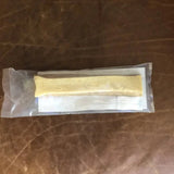 A sealed pouch from Rogue Pet Feed contains a rectangular yellowish Yak Stick high-protein dog treat, placed on folded white paper and set on a brown leather surface.