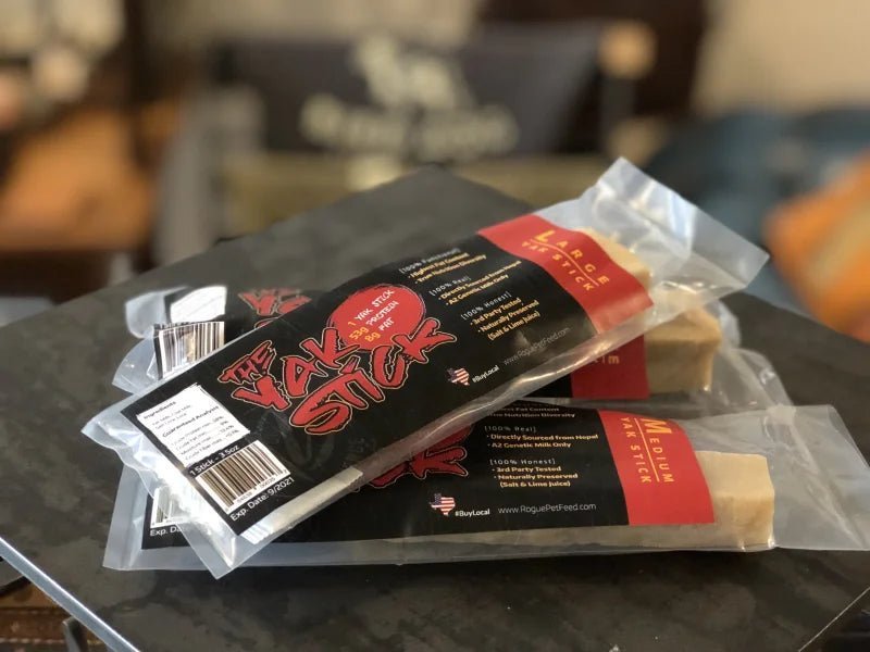 Three Yak Stick | Rogue Pet Feed dog chews are stacked on a dark surface, featuring Rogue Pet Feed branding. These high protein treats are ideal for rewarding your pup.