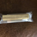 The Yak Stick by Rogue Pet Feed is a sealed, cylindrical dog treat made of light-colored material in plastic packaging, shown on a brown leather surface—a high-protein snack for your pup.