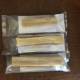 Three vacuum-sealed packages of Rogue Pet Feed Yak Stick dog chews, each containing a single tan, cylindrical stick, are arranged in a vertical row on a brown surface.