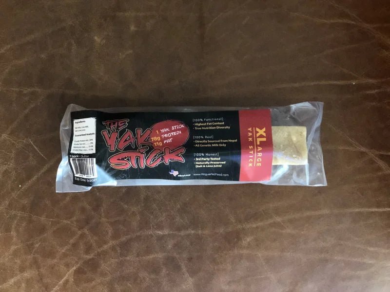 A packaged Yak Stick | Rogue Pet Feed dog chew lies on a brown leather surface. The label emphasizes its high protein content and quality ingredients, establishing it as a premium dog treat from Rogue Pet Feed.